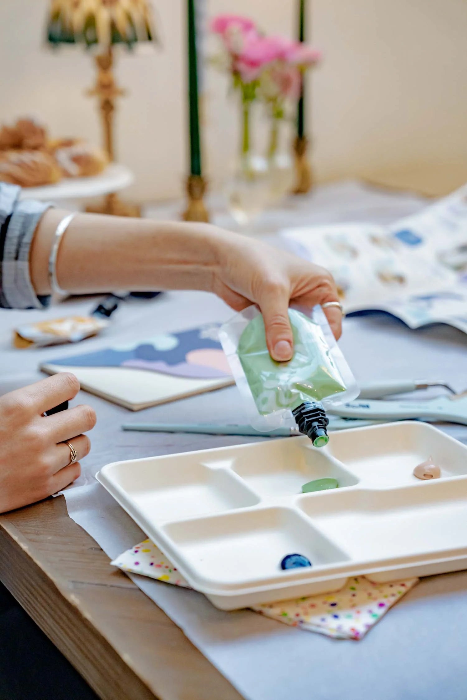 Person holding a small container over a paint palette with canvas art kit
